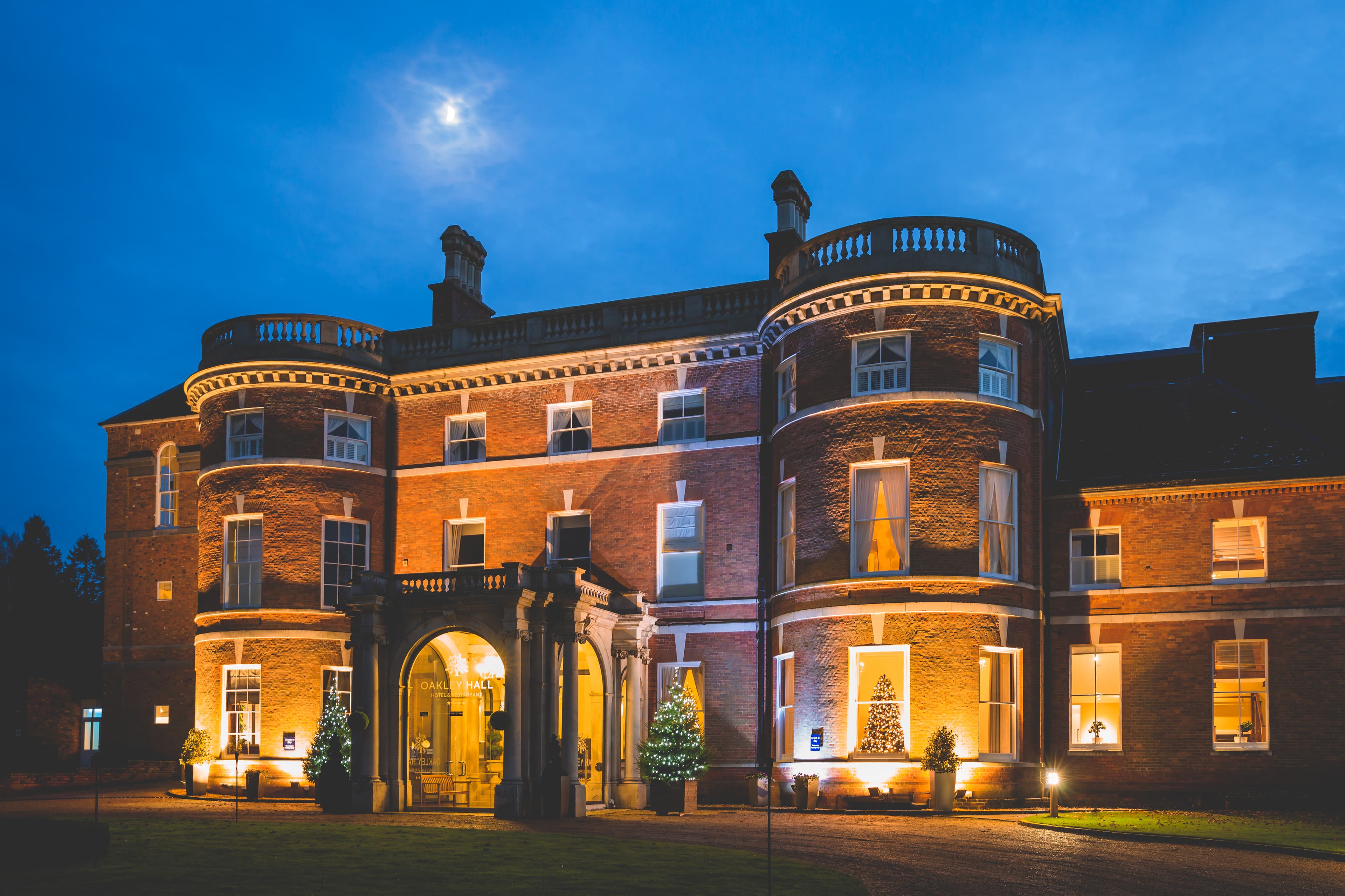 A brick building with extended porch and sweeping drive that is lit up at night.