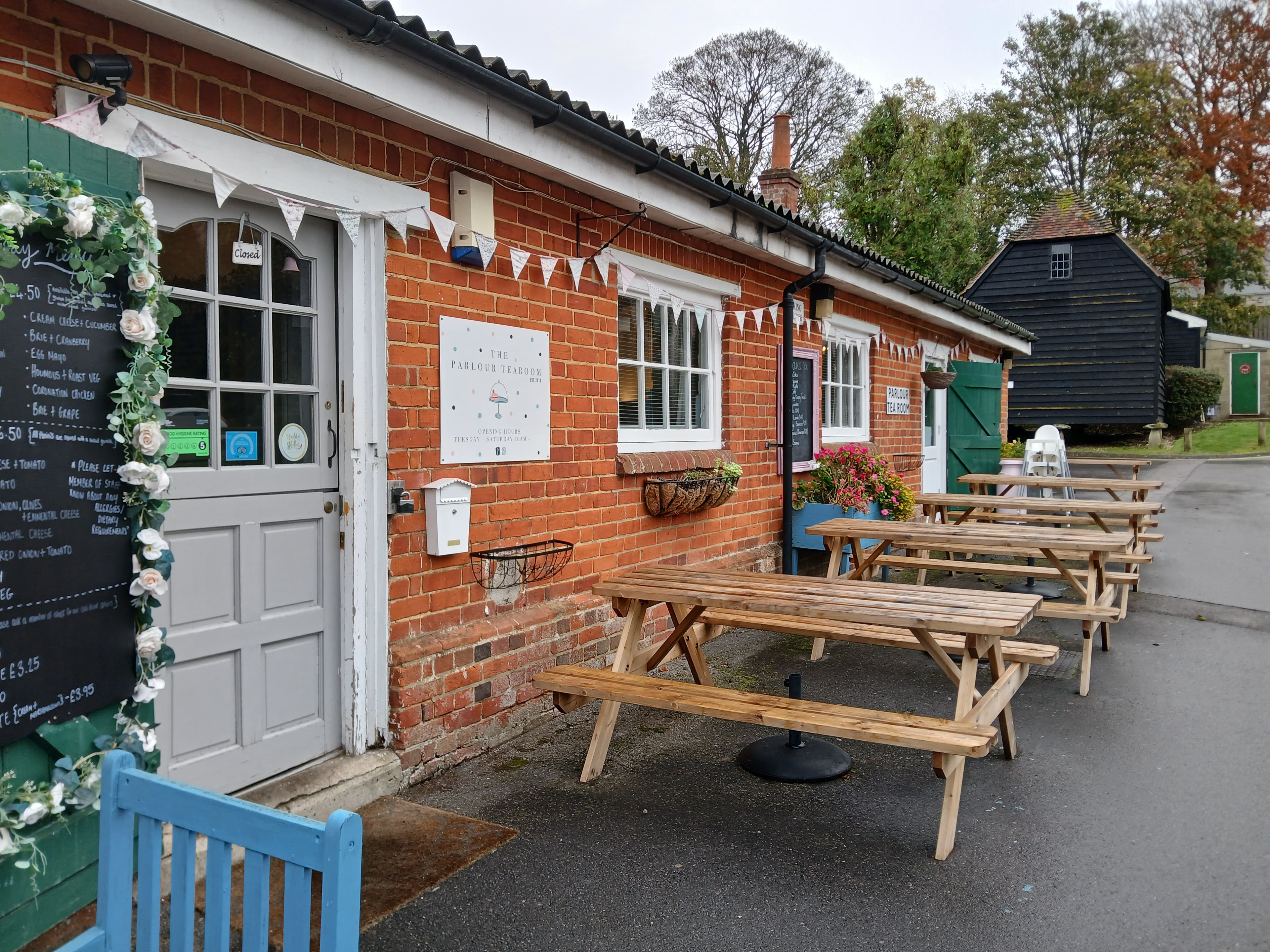 The outside of the Parlour Tearoom. A single storey red brick buidling with tables outside and bunting.